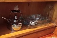 Kettle and Pyrex glass baking dishes inside a wooden cabinet shelf