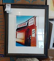 Full view of the framed print depicting the building with sign 'Topless Show Girls' and 'Happy Hour'.