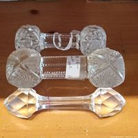 Three vintage glass knife rests on wooden surface; two with ornate pressed glass designs, one faceted octagonal ends