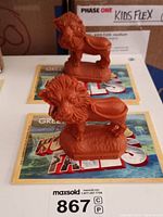 Pair of reddish-brown plastic lion figurines with smooshed faces and the text 'WONDER FALLS' on their bases, displayed on a Wonder Falls postcard.