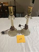 Two matching antique glass table lamps with hobnail bases, brass sockets, and brown cords on white cloth background.
