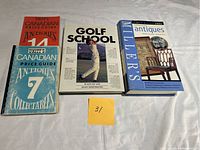 Four books laid out on a flat surface consisting of three Canadian antiques and collectibles price guides and one golf instruction book.