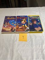 Front cover of three VHS tapes: Aladdin, Pinocchio, and Matilda on white cloth background