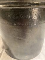 Close-up of embossed maker's mark: 'B.S. MFG Co. LTD, BRANTFORD' on dark glazed crock surface.