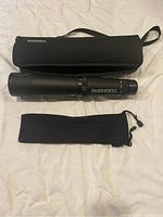 Bushnell spotting scope laid out with zippered carrying case and soft pouch on light fabric background.