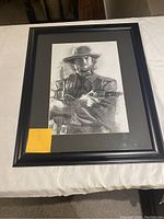 Frontal view of framed charcoal portrait showing Clint Eastwood in cowboy attire holding two revolvers.