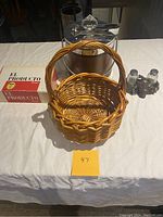 Photo showing ice bucket with lid, wooden empty cigar box labeled El Producto, wicker basket, and salt and pepper shakers with holster on table.