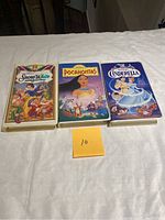 Front view of three Disney VHS movies showing the cover art for Snow White, Pocahontas, and Cinderella in white plastic cases on a white surface.