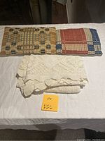 Two small pillows with geometric woven fabric, earth-tone colors, and the white lace tablecloth folded underneath with a note showing dimensions