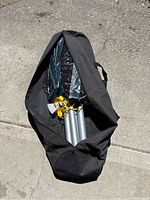 Overhead shot of badminton net set partially pulled out of black carry bag, showing folded net inside green sleeve, two silver poles, two white shuttlecocks and yellow cords.