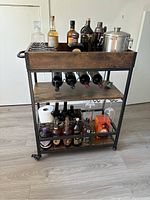 Front view of bar cart with bottles, wine rack, and top shelf with bottles and ice bucket (contents not included).
