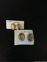 Two pairs of oval Birks sterling silver earrings mounted on white card stock, showing relief detail on front surfaces.