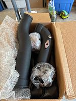 New matte black charge pipe in box with additional hardware wrapped in plastic bags.