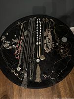 Overview of multiple assorted costume jewelry necklaces laid out on a black surface, showing variety of styles, colors, and pendants.