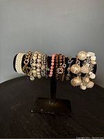 Photo of assorted bead and pearl bracelets displayed on black stand on black table against gray background.