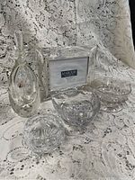 Clear glassware collection on lace background, featuring Marquis by Waterford crystal picture frame with label visible, tall perfume bottle with stopper, and three small cut glass bowls and dishes.