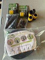 Photo of assorted drip irrigation components including stakes, tubing, connectors, two sealed adapter sets in original packaging, and a user manual.