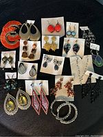 Photo showing the entire assorted lot of 21 pairs of earrings in various styles and colors including beaded hoops, dangling drops, studs, and chandelier types.