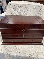 Closed view of the dark-polished wooden jewelry box with metal keyhole lock and two small drawers with metal knobs at the bottom.