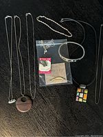 Photo of assorted silver and gold plate jewelry on a dark surface including various necklaces, bracelet, bangle, and pendants in bag.