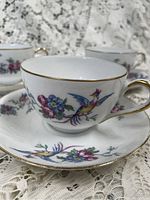 Close-up photo of one teacup and its saucer showing floral and bird design with gold trim