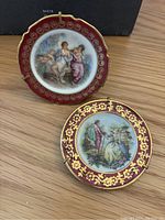 Two Limoges decorative mini plates photographed showing the front designs and holding frames; one frame is visibly damaged.