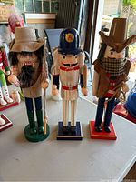 Photo showing three nutcrackers on a table, each with distinct themes: fisherman, baseball player, and cowboy.