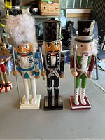 Three wooden nutcrackers arranged side by side on a gray surface showing front view and intricate costume details.