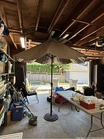 Full view of patio umbrella standing open inside a garage with assorted items around.