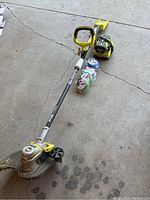 Full shot of the RYOBI weed wacker with battery pack, charger, and multiple spools of trimmer line laid on a concrete floor.