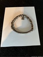 Single silver bracelet laid on a white card with visible beads and silver bar.