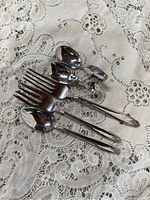 Photo shows two standard silver-colored forks, two regular spoons, and two smaller sterling baby spoons arranged on lace fabric.