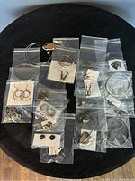 View of assorted silver jewelry laid out individually in small clear plastic bags on a round black table, including earrings, bracelets, and pendants.