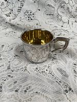 Side view of sterling silver cup with gold interior on lace fabric background.