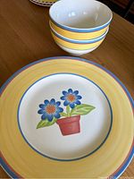 Photo showing two cereal bowls stacked with a dinner plate featuring a floral pot design and yellow rim underneath.