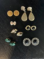 Top view of 7 pairs of assorted vintage clip on earrings on black background showing designs and colors