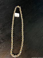 Photo showing a vintage necklace with clear and gold-tone faceted beads along a black background, with matching earrings attached to a white card.