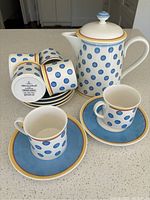 Full view of 6 demitasse cups stacked on matching saucers with coffee pot, showing blue polka dot pattern and color accents