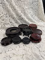 Photo showing an assortment of 11 wooden plant and vase stands of different sizes and finishes, placed on white lace fabric