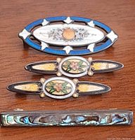 Top down image of all four antique brooch bars displayed together on wooden surface showing details of each item