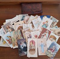 Full view of the collection of antique holy prayer cards spread out on a wooden surface, with a brown leather pouch behind them.