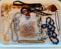 Full view of costume jewellery assortment in a plastic container including faux pearl necklaces, beaded necklaces in various colors, and loose beads.