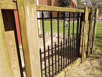 Close-up of wrought iron insert with pointed finials framed in pressure treated wood with vertical slats