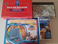 Four games in original boxes arranged on a surface: Balderdash, Card and Dice Games Gift Set, Super Sink the Fleet, and Boggle Deluxe.