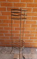 Full view of the gold tone metal plant stand against a brick wall, showing height and structure.