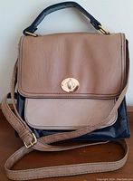 Front view of the purse showing tan flap, shoulder strap, and top handle.