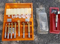 Wooden box with seven gold Forstner drill bits laid out with protective end caps on yellow foam