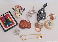 Photo showing an assortment of 11 vintage ladies brooches in varied shapes and materials.