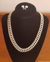 Full view of necklace and earrings displayed on black jewelry stand, showing design and size