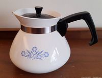 Full side view of the vintage Corning Ware Blue Cornflower tea pot showing the blue floral pattern, black handle, and stainless steel band.